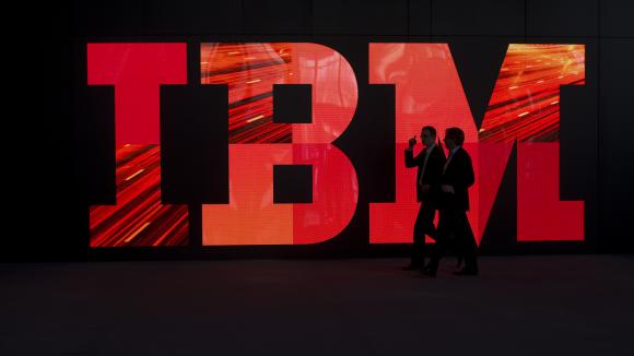 Deux hommes passent devant le logo IBM sur un mur.