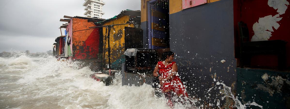 Les vagues Ã©claboussent une femme devant des maisons cÃ´tiÃ¨res lors d\'une marÃ©e haute Ã  Bombay, en Inde, le 4 juillet 2019.