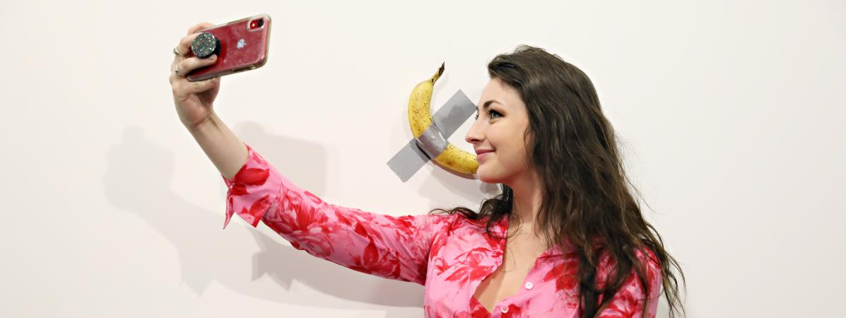 Une jeune femme prend un selfie avec l\'oeuvre \"The comedian\" de Maurizio Cattelan, une simple banane scotchée au mur, à la foire d\'art contemporain Art Basel de Miami, le 6 décembre 2019.