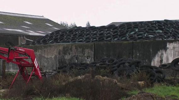 Des pneus entassés dans un champ agricole.