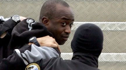 Youssouf Fofana est escorté par deux policiers pour le ramener à Paris en avion,&nbsp;le 4 mars 2006 à Abidjan (Côte-d'Ivoire). (ISSOUF SANOGO / AFP)