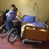 Une aide à domicile aide un homme hémiplégique à s'asseoir dans sa chaise roulante, le 7 février 2003, à Secqueville-en-Bessin (Calvados). (MYCHELE DANIAU / AFP)