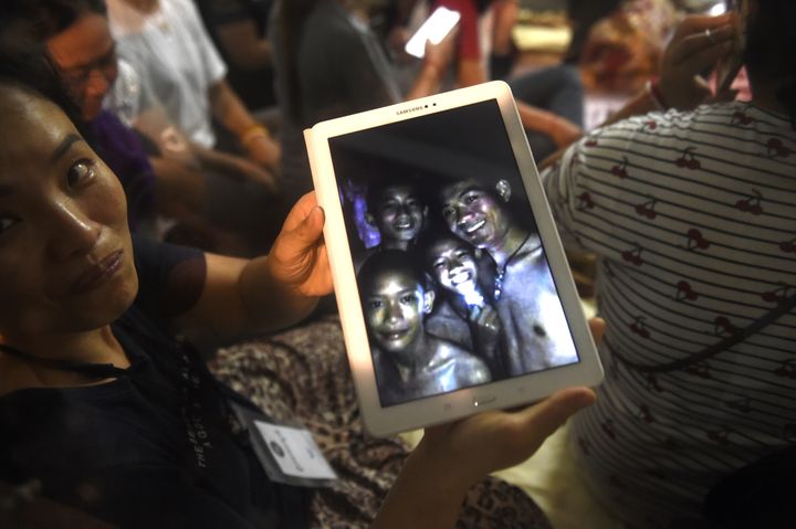 Une membre de la famille d'un des enfants disparus dans la grotte de Tham Luang (Thaïlande) regarde une photo de quatre de ces rescapés après leur découverte, le 2 juillet 2018. (LILLIAN SUWANRUMPHA / AFP)