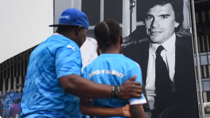 Des Marseillais se recueillent devant une photo en noir et blanc de Bernard Tapie, installée devant le Vélodrome (Bouches-du-Rhône), le 3 octobre 2021. (CLEMENT MAHOUDEAU / AFP)