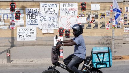 Un livreur passe devant des affiches réclamant le retour des otages détenus par le Hamas, à Tel-Aviv, en Israël, le 22 octobre 2023. (NIR KEIDAR / ANADOLU / AFP)