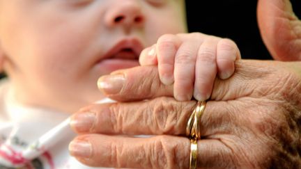 Un bébé tient la main d'une personne agée. (SYLVIE CAMBON / MAXPPP)