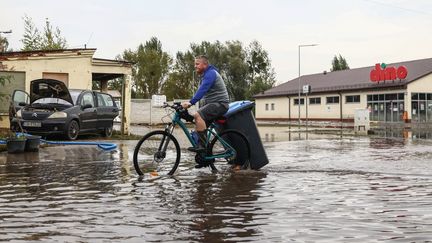 Un homme à vélo transporte une poubelle dans une rue inondée à Lewin Brzeski (Pologne), le 23 septembre 2024. (BEATA ZAWRZEL / NURPHOTO / AFP)