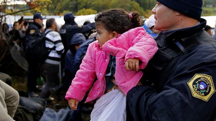 Un officier de police slov&egrave;ne prot&egrave;ge une petite fille tandis qu'un flot de migrants tente de briser un cordon de police pr&egrave;s de la fronti&egrave;re autrichienne &agrave; Sentij, en Slov&eacute;nie, le 2&agrave; octobre 2015. (? LEONHARD FOEGER / REUTERS )