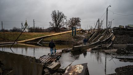 Des habitant de Bakhmut, le 6 janvier 2023, sur un pont détruit par les bombardements. (DIMITAR DILKOFF / AFP)