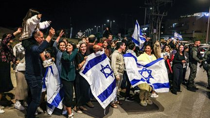 Israelis wave flags and applaud after a vehicle carrying hostages released by Hamas passes towards a military base in Ofakim, southern Israel, on November 26, 2023. (MENAHEM KAHANA / AFP)