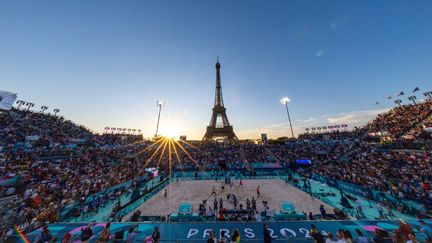 Qui dit mieux pour une soirée d'été ? Le soleil se couche sur la tour Eiffel et le terrain de beach volley installé sur le Champ-de-Mars, le 28 juillet 2024. (AYTAC UNAL / ANADOLU / AFP)