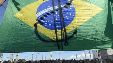 Un drapeau br&eacute;silien barr&eacute; par un dollar est d&eacute;ploy&eacute; par des manifestants devant les forces de police avant un match de football opposant le Mexique au Br&eacute;sil &agrave; Fortaleza (Br&eacute;sil), le 19 juin 2013. (REUTERS)