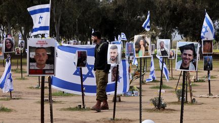 Un soldat israélien marche au milieu des portraits de victimes ou d'otages retenus depuis le 7 octobre dans la bande de Gaza par le Hamas, à Re'im (Israël), le 14 janvier 2024. (MENAHEM KAHANA / AFP)