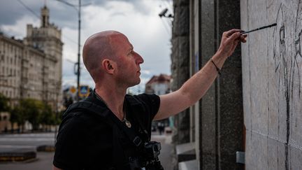 L'artiste de rue ukrainien Gamlet Zinkivskyi peint sur une planche de bois dans une rue de Kharkiv, le 16 mai 2022, en pleine invasion de l'Ukraine par la Russie. (DIMITAR DILKOFF / AFP)