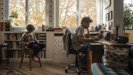 Un père télétravaille en présence de son enfant, le 14 novembre 2020 à Toulouse (Haute-Garonne). (CELINE GAILLE / HANS LUCAS / AFP)