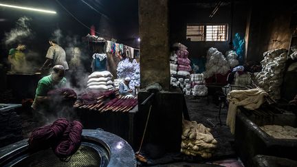 Dans une atmosphère baignée de vapeur, les ouvriers s'activent autour des grands bains chauds d'eau colorée. Ils démêlent les longs fils de coton, les suspendent sur des perches en bois avant de les plonger dans les bassines fumantes.&nbsp; &nbsp; &nbsp;&nbsp; (KHALED DESOUKI / AFP)