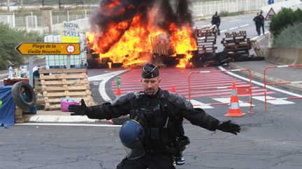 Un gendarme empêche l'accès à une barricade en feu, pendant que ses collègues dispersent les "gilets jaunes" qui bloquent le dépôt de pétrole de&nbsp;Port-La-Nouvelle (Aude), le 20 novembre 2018. (RAYMOND ROIG / AFP)