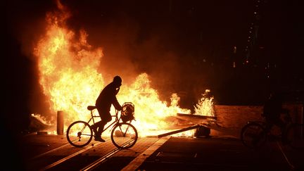 Un personne à vélo passe près d'un brasier allumé pendant la manifestation des "gilets jaunes" à Bordeaux (Gironde), le 8 décembre 2018.&nbsp; (NICOLAS TUCAT / AFP)