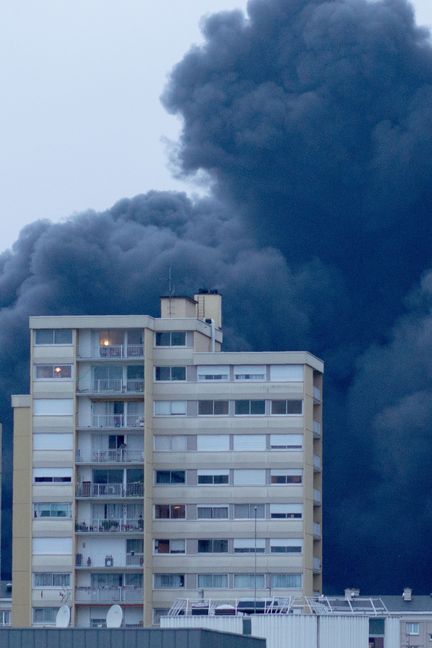 Derrière des immeubles, la fumée noire qui s'échappe de l'usine Luzibrol à Rouen, le 26 septembre 2019. (THIBAUT DROUET / AFP)