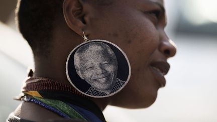 Une Sud-africaine portant des boucles d'oreille &agrave; l'effigie de l'ancien pr&eacute;sident Nelson Mandela se tient devant l'hopital o&ugrave; se dernier se trouve dans un &eacute;tat critique &agrave; Pr&eacute;toria (Afrique du Sud), le 26 juin 2013. (FILIPPO MONTEFORTE / AFP)