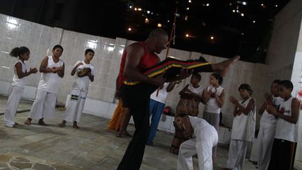 La capoeira est liée à l’histoire de la traite des Noirs africains et de l’esclavage sur les côtes brésiliennes. «Pour résister et s’affranchir, (les esclaves) ont développé, en secret, une forme de lutte, déguisée en danse : la capoeira», raconte le site vidadecapoeira.com. Aujourd’hui, celle-ci «est une pratique culturelle (…) qui relève à la fois du combat et de la danse et peut être considérée comme une tradition, un sport et même une forme d’art. Les capoeiristes forment un cercle au centre duquel deux d’entre eux s’affrontent. Les mouvements exécutés exigent une grande souplesse du corps. Les autres capoeiristes autour du cercle chantent, tapent des mains et jouent d’instruments à percussion», explique le site de l’Unesco. Ici, un professeur de capoeira aveugle, Joao Kanoa, initie des éllèves au fameux cercle dans une favela de Rio de Janeiro, le 26 avril 2013.  (REUTERS - Pilar Olivares)