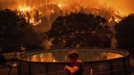Une femme dans le jardin de sa maison, à Klamath (Californie) alors que l'incendie baptisé "McKinney" fait rage, le 30 juillet 2022. (NOAH BERGER / AP / SIPA)