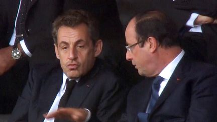 Nicolas Sarkozy et Fran&ccedil;ois Hollande discutent le 10 d&eacute;cembre 2013 dans les gradins du stade de Johannesbourg (Afrique du Sud) lors d'une c&eacute;r&eacute;monie d'hommage &agrave; Nelson Mandela. (SABC / AFP)