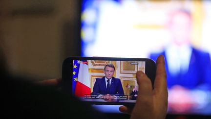 Une personne regarde l'allocution d'Emmanuel Macron sur son téléphone portable, le 5 décembre 2024. (VINCENT VOEGTLIN / MAXPPP)