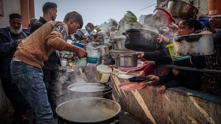 Des Palestiniens attendent lors d'une distribution de nourriture dans un camp de réfugiés à Rafah, dans le sud de la bande de Gaza, le 23 décembre 2023. (SAHER ALGHORRA / MIDDLE EAST IMAGES / AFP)