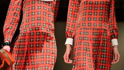 C'est une femme au caractère trempé qui défile chez Moschino, affichant es origines écossaises. Le tartan, avec ses gros carreaux rouges et noirs, domine cette collection, des manteaux courts aux tailleurs mini-kilt, en passant par les costumes trois pièces et jusque dans les longues robes de soirées. Rien ne manque à la panoplie du traditionnel costume écossais: de la petite sacoche portée à la ceinture sur le devant de la jupe au calot noir orné d'un pompon rouge, rubans flottants à l'arrière. Les chaussettes en laine sont de rigueur, quant aux pattes en cuir qui servent habituellement à attacher le kilt, elles sont utilisées à la place des boutons pour fermer les vestes. L'habit se porte sur une chemise blanche, éventuellement agrémentée d'un jabot, toujours avec le gilet, noud papillon en option. Les vêtements sont soignés dans les moindres détails: martingale derrière le manteau, revers des vestes en velours, coudières bordées d'un galon. Mais cette rigueur est égayée d'énormes emblèmes dorés et de grands cours entrelacés de roses brodés ici et là sur les vêtements.
 (GIUSEPPE CACACE /AFP)