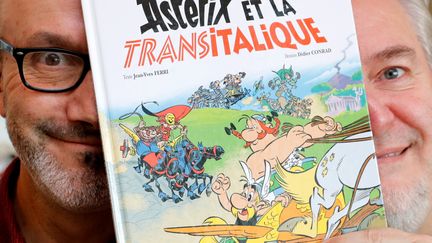 Jean-Yves Ferri et Didier Conrad, les auteurs de l'album "Astérix et la Transitalique", posent derrière la couverture, le 17 octobre 2017 à Vanves (Hauts-de-Seine). (PHILIPPE WOJAZER / X00303)