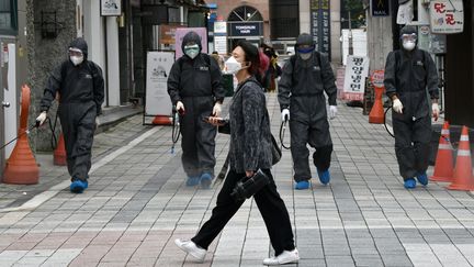 Une femme passe devant des responsables sanitaires sud-coréens pulvérisant des désinfectants dans un quartier commercial d'Incheon dans le nord du pays, le 17 septembre 2020 (photo d'illustration). (JUNG YEON-JE / AFP)