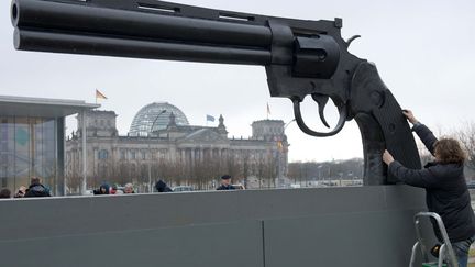 Des militants pacifistes installent un pistolet g&eacute;ant devant la Chancellerie &agrave;&nbsp;Berlin (Allemagne) sur lequel est inscrit "Nos armes tuent, l'Allemagne est le 3e exportateur mondial d'armes", le 25 f&eacute;vrier 2013. (MAURIZIO GAMBARINI / DPA / AFP)