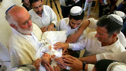 Un nouveau-n&eacute; tout juste circoncis est b&eacute;ni lors d'une c&eacute;r&eacute;monie&nbsp;dans une synagogue de Ganei Tal, dans la bande de Gaza, le 4 mai 2005. (DAVID FURST / AFP)