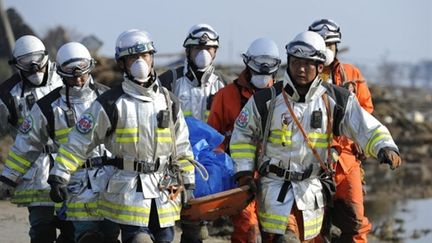 Des secouristes portent un cadavre, dimanche 13 mars à Sendaï. (AFP - Philippe Lopez)