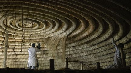 Des artisans fixent les anneaux circulaires au plafond de l'un des bâtiments appartenant aux tombeaux royaux de Kasubi à Kampala, en Ouganda, le 13 juin 2023. (STUART TIBAWESWA / AFP)