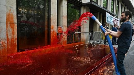 Un militant d'Extinction Rebellion asperge de faux sang le bâtiment&nbsp;du Medef, à Paris, le 19 juin 2020. (BERTRAND GUAY / AFP)