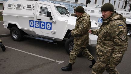 Des soldats ukrainiens passent devant des véhicules blindés de la mission de l'OSCE en Ukraine, le 12 novembre 2014, à Kiev. (VLADIMIR SHTANKO / ANADOLU AGENCY / AFP)