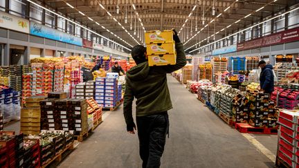 Un marchand transporte des caisses de fruits au pavillon des fruits et légumes du marché international de Rungis (Val-de-Marne ), le 6 décembre 2023. (DIMITAR DILKOFF / AFP)