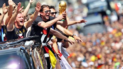 Des joueurs de l'&eacute;quipe de football d'Allemagne brandissent la Coupe du monde depuis le bus qui leur fait traverser Berlin pour c&eacute;l&eacute;brer leur victoire au Mondial, mardi 15 juillet 2014. (JAN WOITAS / AFP)