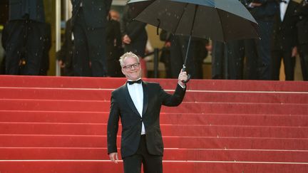 Puisqu'il ne peut rien faire face &agrave; la pluie qui trempe son festival, Thierry Fr&eacute;maux,&nbsp;le d&eacute;l&eacute;gu&eacute; g&eacute;n&eacute;ral, a d&eacute;cid&eacute; d'accueillir lui m&ecirc;me ses invit&eacute;s avec un parapluie. Une mani&egrave;re comme une autre de se faire pardonner le mauvais temps. (ALBERTO PIZZOLI / AFP)