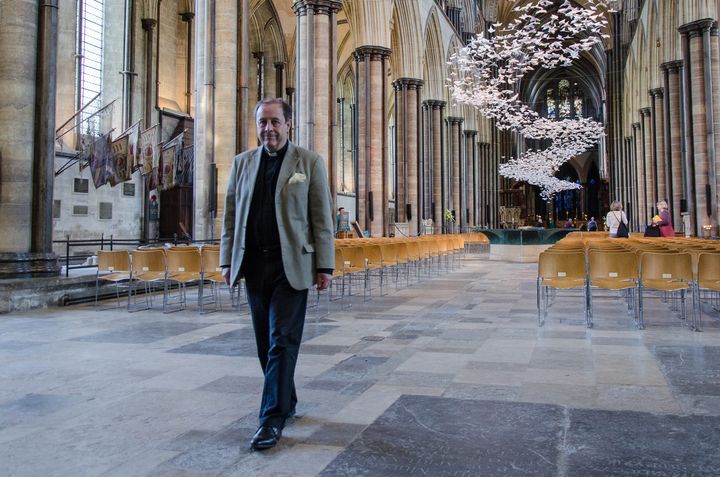 Le chanoine Robert Titley pose devant l'installation "Les Colombes", le 14 mai 2018, dans la cathédrale de Salisbury. (YANN THOMPSON / FRANCEINFO)