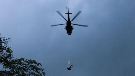 Pour acheminer du matériel, des hélicoptère survolle constamment la zone. Ici, un&nbsp;appareil de l'armée thaïlandaise&nbsp;transporte une pelleteuse.&nbsp; (PATIPAT JANTHONG / BANGKOK POST)