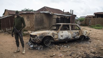 Un membre des forces de sécurité nigériane se tient à côté d'un véhicule incendié dans le village de Nghar, près de Jos, le 27 juin 2018, après l'attaque de bergers Fulani contre des fermiers chrétiens de l'ethnie Berom, qui avait fait 84 morts. (STEFAN HEUNIS / AFP)