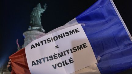 Lors du rassemblement contre l'antisémitisme place de la République à Paris, le 19 février 2019, un homme brandit un drapeau français sur lequel on peut lire "Antisionisme = antisémitisme voilé".&nbsp; (ANTONI LALLICAN / HANS LUCAS / AFP)