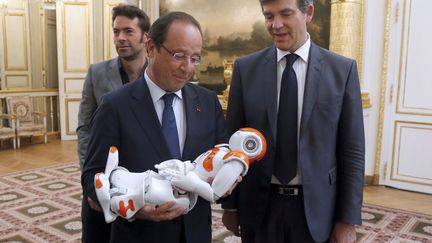 Le pr&eacute;sident fran&ccedil;ais Fran&ccedil;ois Hollande (C) et le ministre du Redressement productif, Arnaud Montebourg (D) rencontrent&nbsp;le robot Nao&nbsp;dans le cadre de la pr&eacute;sentation de 34 plans destin&eacute;s &agrave; construire "la Nouvelle France industrielle" au palais de l'Elys&eacute;e &agrave; Paris, le 12 septembre 2013. (CHARLES PLATIAU / AFP)