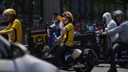 Une livreuse boit de l'eau au milieu du trafic en attendant de traverser la rue à Pékin (Chine), le 21 juin 2023. (ANDY WONG/ AP / SIPA)