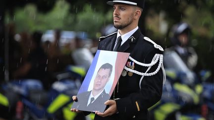 Un gendarme tient le portrait d'Éric Comyn durant une cérémonie d'hommage le 3 septembre 2024 à Nice (Alpes-Maritimes), à ce gendarme tué lors d'un contrôle routier à Mougins. (VALERY HACHE / AFP)