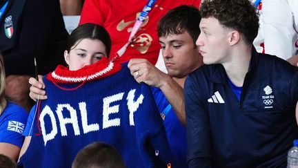 Tom Daley (au centre), en train de tricoter un pull dans les gradins d'épreuves aux Jeux olympiques de Paris, le 27 juillet 2024. (MIKE EGERTON / MAXPPP)