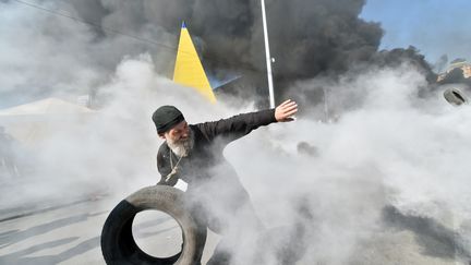 Un pr&ecirc;tre orthodoxe jette un pneu pendant que les derniers activites de la place Maidan, &agrave; Kiev, se heurtent aux services municipaux venus d&eacute;gager la place, jeudi 7 ao&ucirc;t 2014. (SERGEI SUPINSKY / AFP)